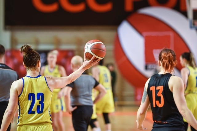 Woman basketball player holding basketball up next to another woman basketball player on the opposing team.
